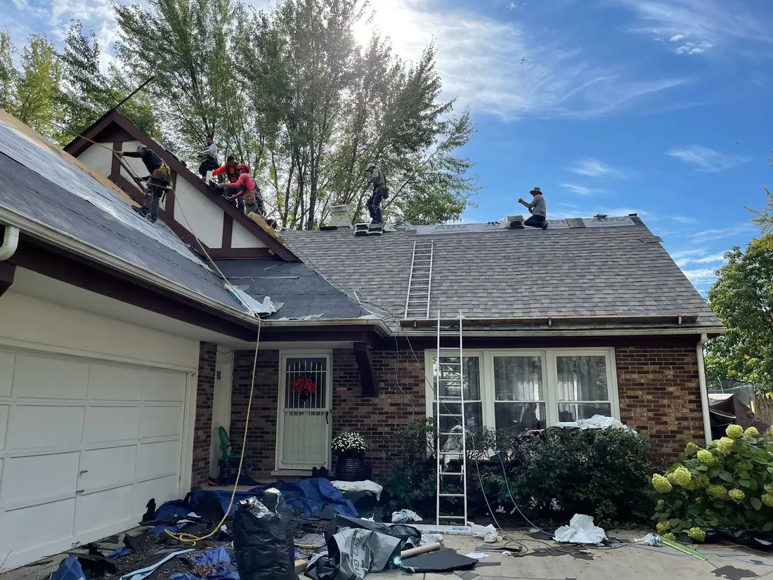 Crew of roofers working along the ridge of a brick and stucco house while old shingles come off