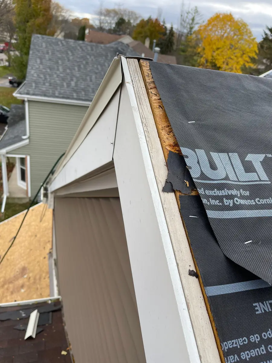 White metal drip edge and synthetic underlayment along a rake edge, with the gable trim below