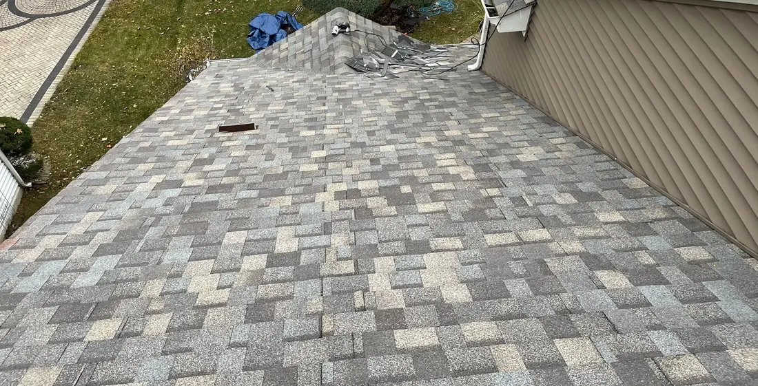 Newly shingled roof meeting a wall of tan vinyl siding, seen from above with the front yard below