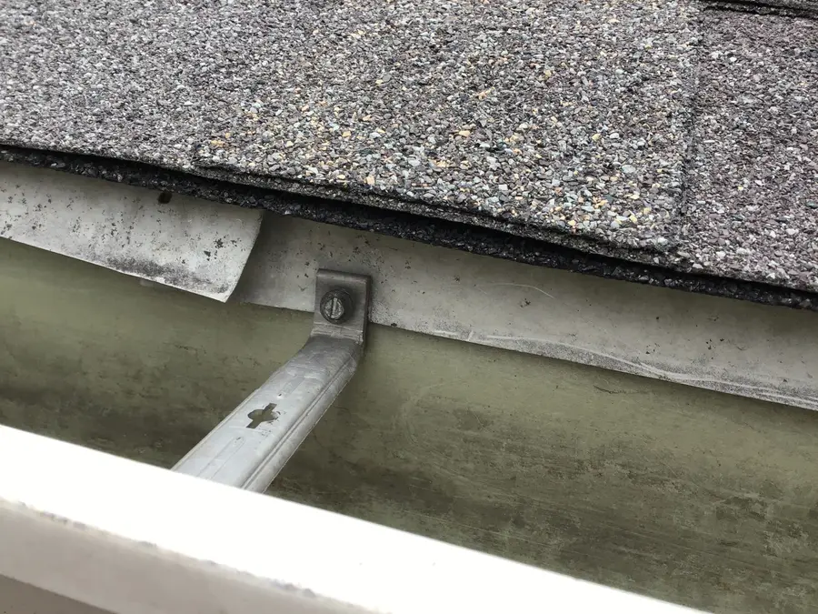 Close-up inside an old aluminum gutter showing a hanger screwed through the drip edge