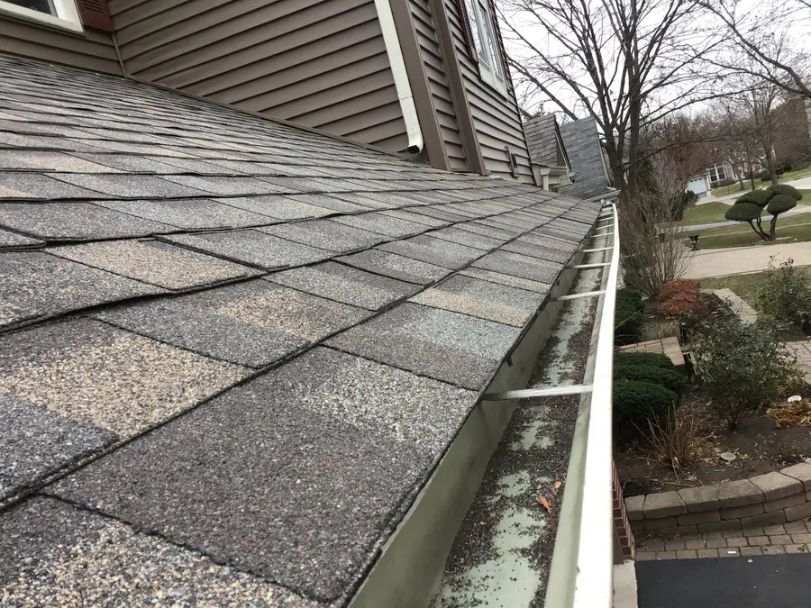 Old gutter along a worn asphalt shingle roof edge, with grit and debris lying in the trough