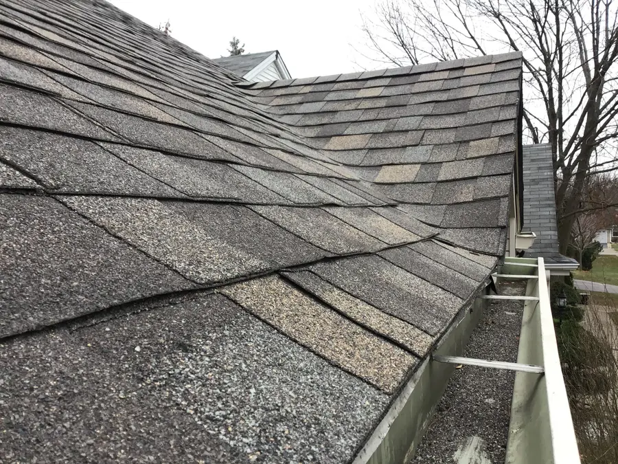 Old shingles where a roof valley meets the eave, above a gutter full of grit