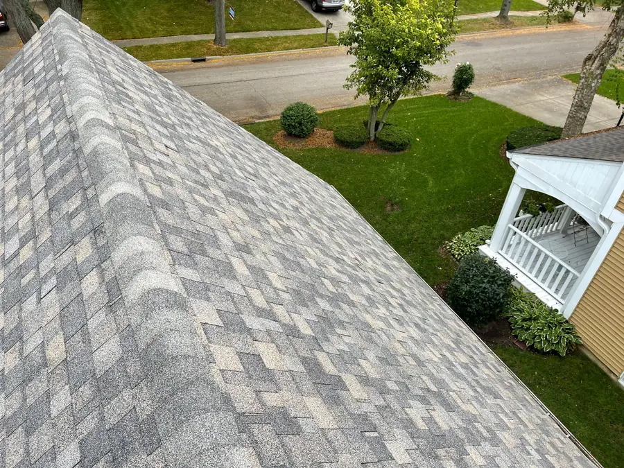 Peak of a new shingle roof seen from above with the street, a lawn and a white porch below