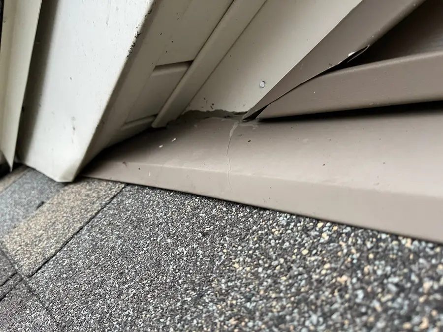 Close-up of a bent metal kick-out flashing where a roof edge meets tan siding and trim