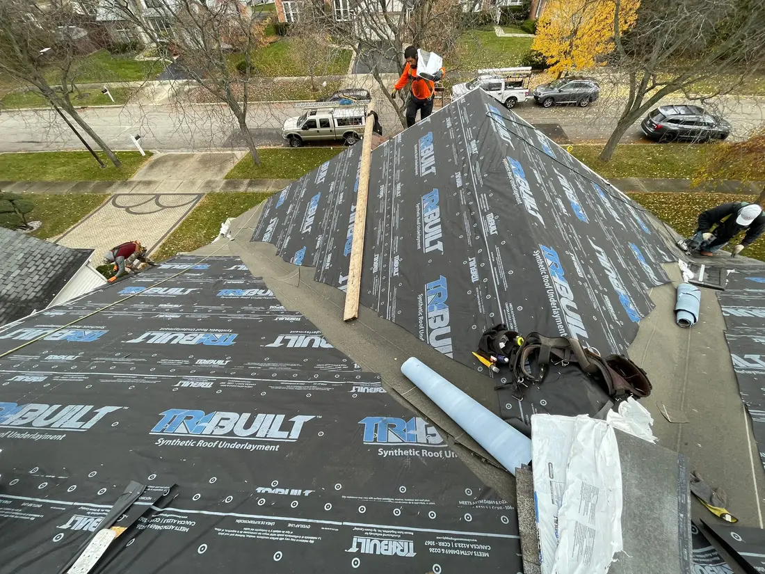 Roof covered in synthetic underlayment up to the ridge, with roofers, bundles and tools along the peak