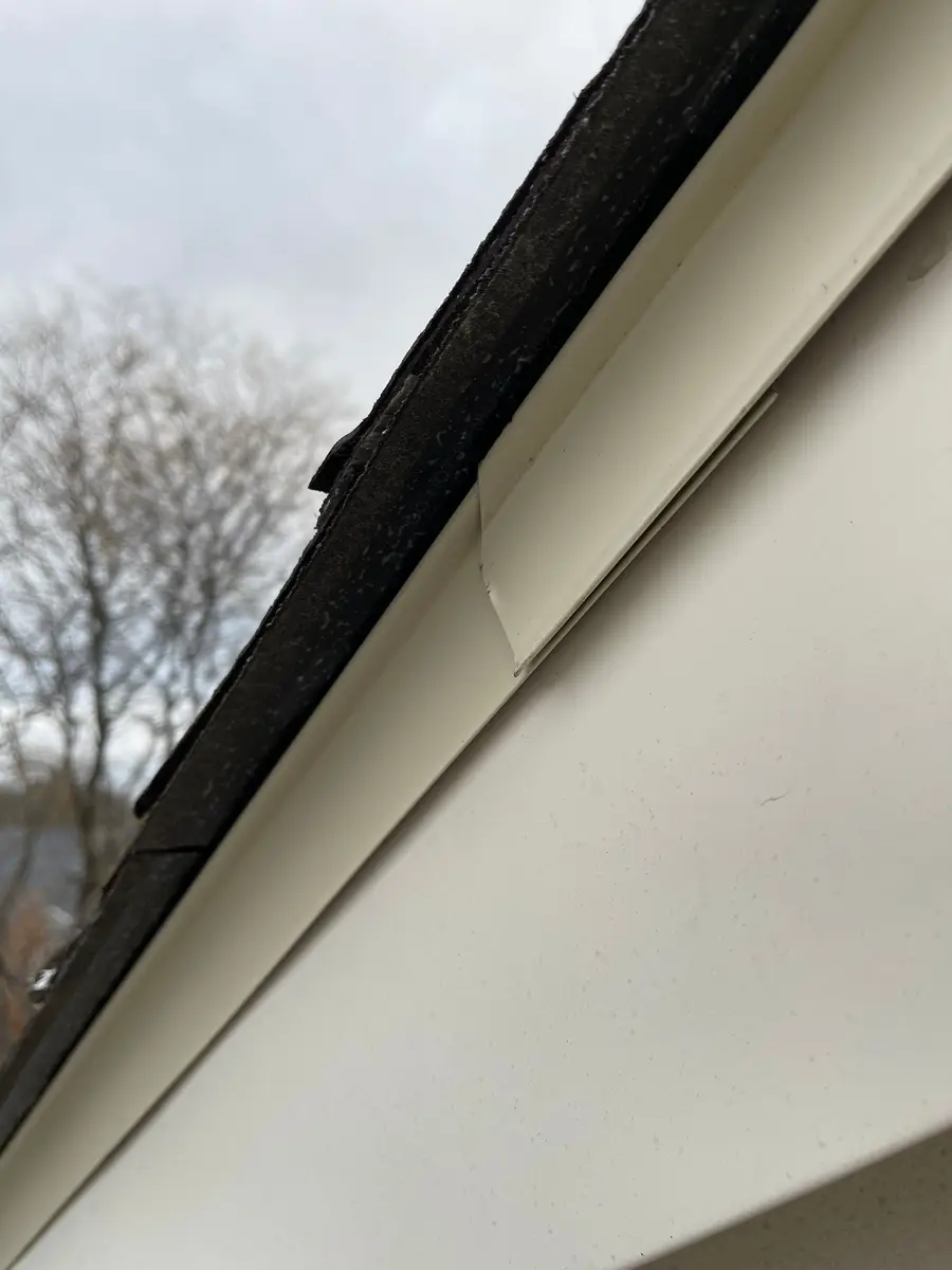 Underside of a roof edge seen from below with white fascia and soffit against a cloudy sky