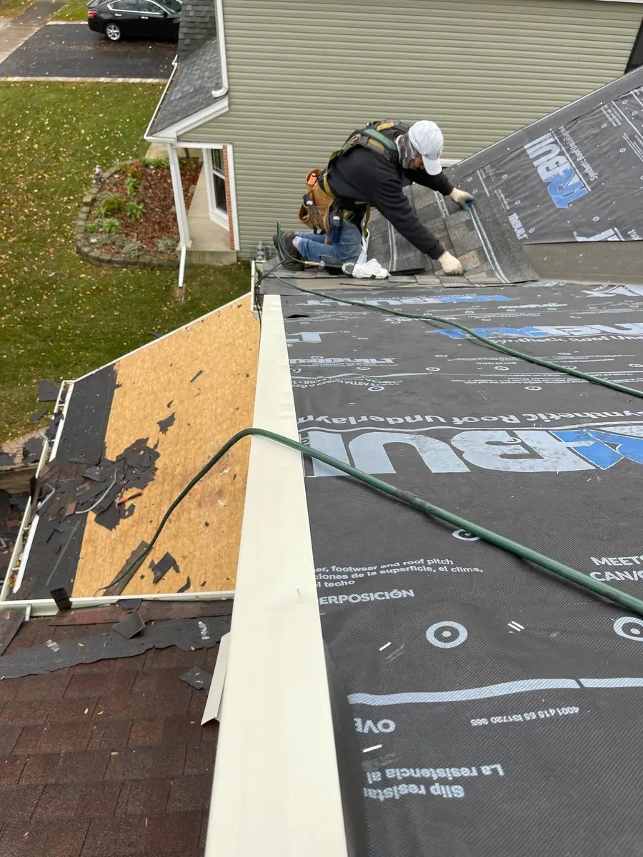 Roofer in a white cap nailing the first shingles at a roof edge over synthetic underlayment