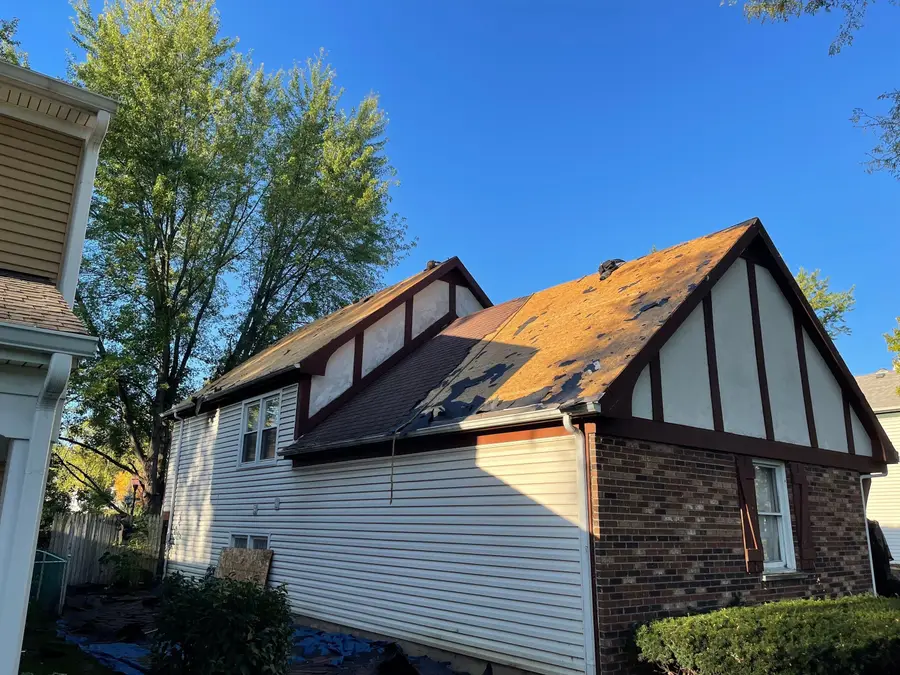 Side of a brick and stucco house with the old roof half stripped to the wood deck on a sunny day
