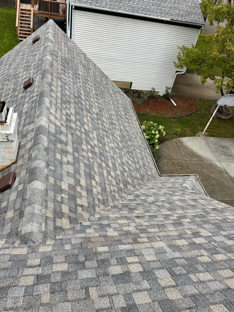 Two new shingle slopes meeting at an open valley beside white vinyl siding